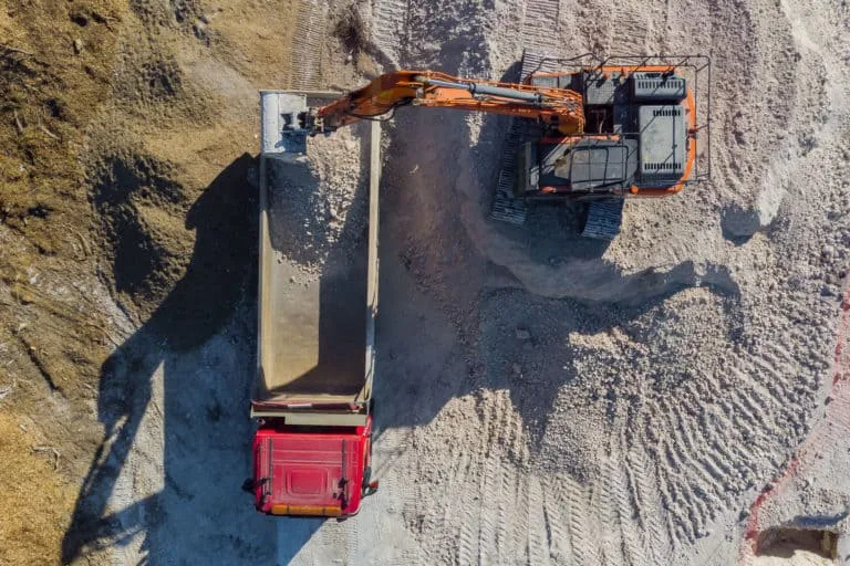 Excavator loading gravel into a truck at construction site.