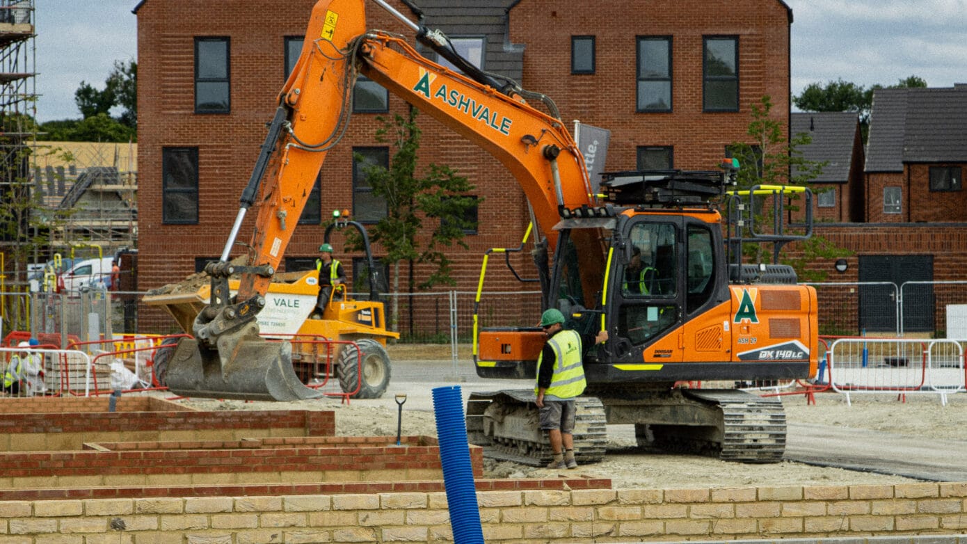 Excavator on construction site with workers nearby.